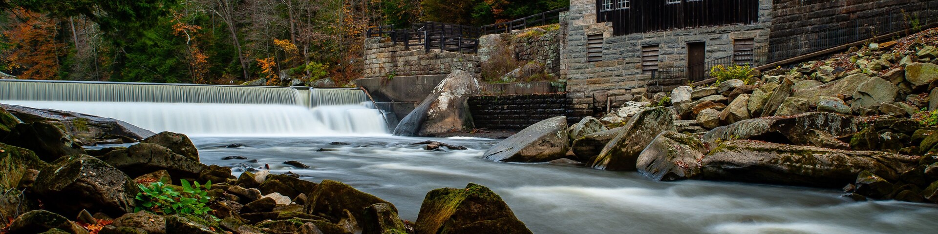 A waterfall, a stone building, and autumn foliage.