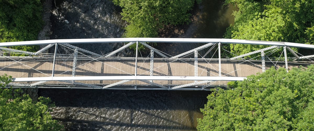 An aerial view of a steel bridge over a river, surrounded by dense green foliage.