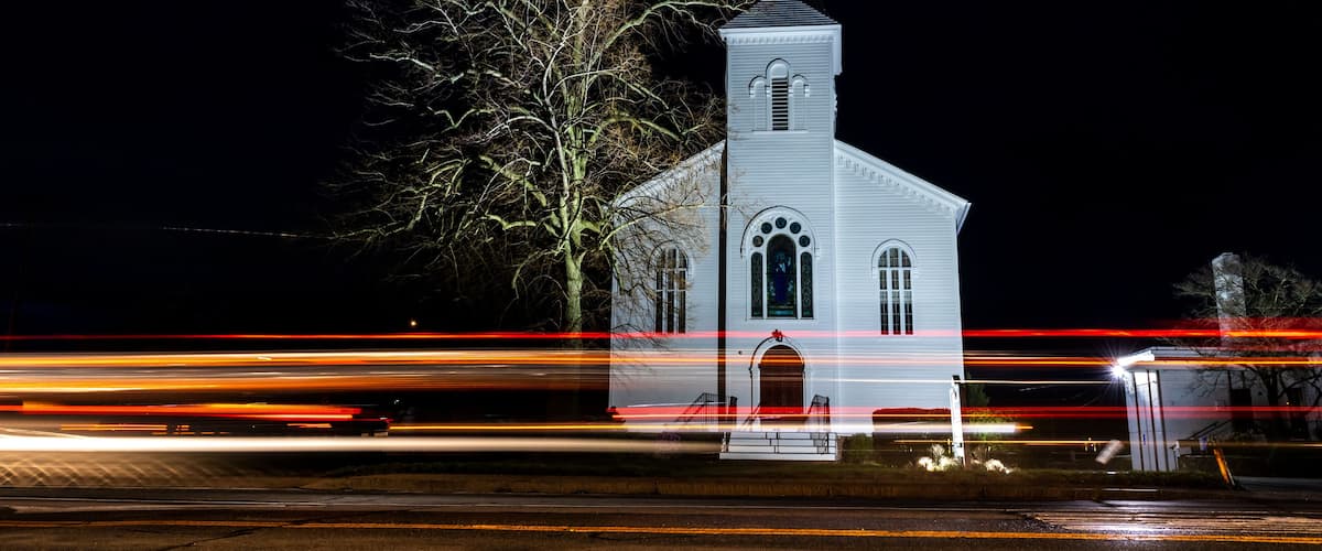 Une église blanche, dotée d’un flèche pointue, de nuit.