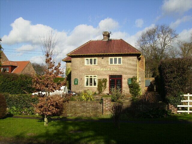 A two-story brick house with a red tiled roof, a red door, and a small garden with a white picket fence.