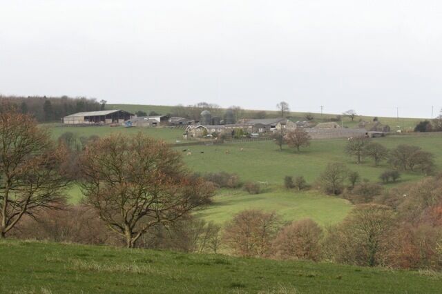 A rural landscape with rolling hills, scattered trees, and farm buildings.