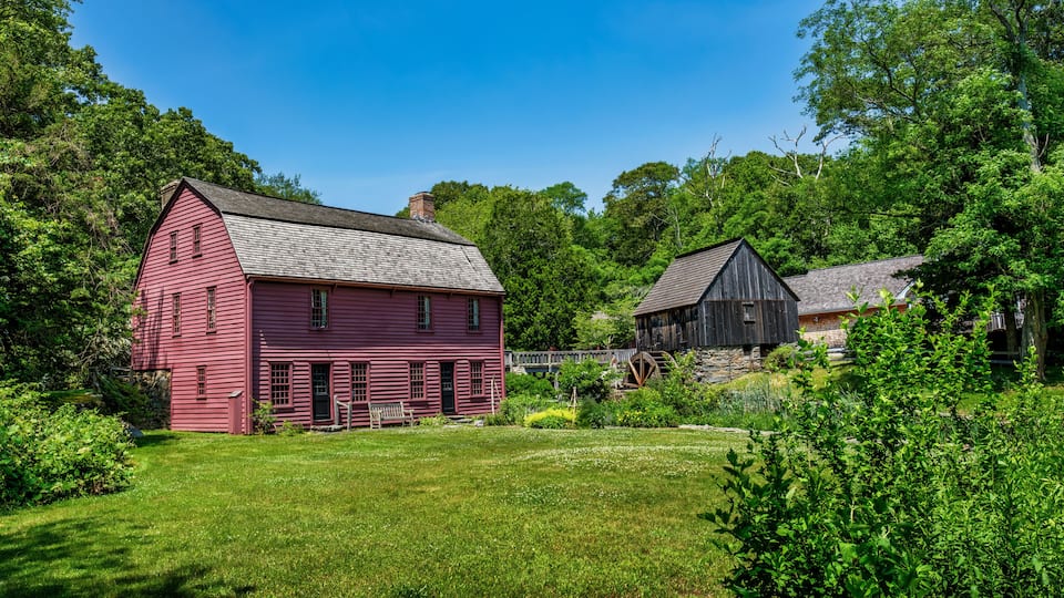 A red barn and a black barn in a lush green field with trees in the background.