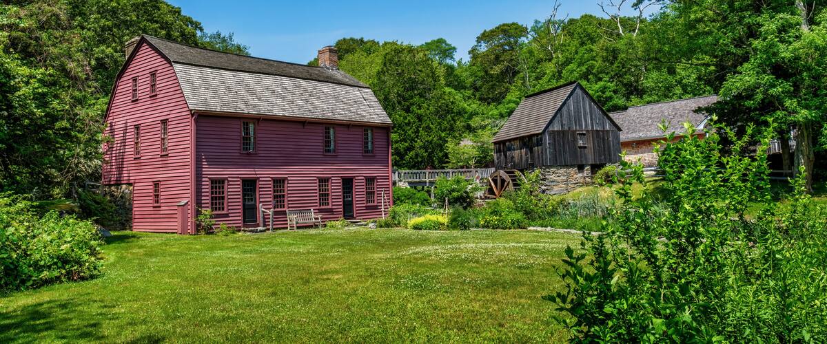 A red barn and a black barn in a lush green field with trees in the background.