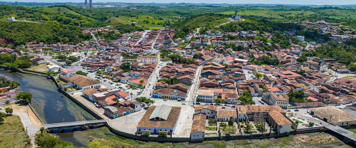An aerial view of a historic town with a river, a fortified wall, and a prominent church.