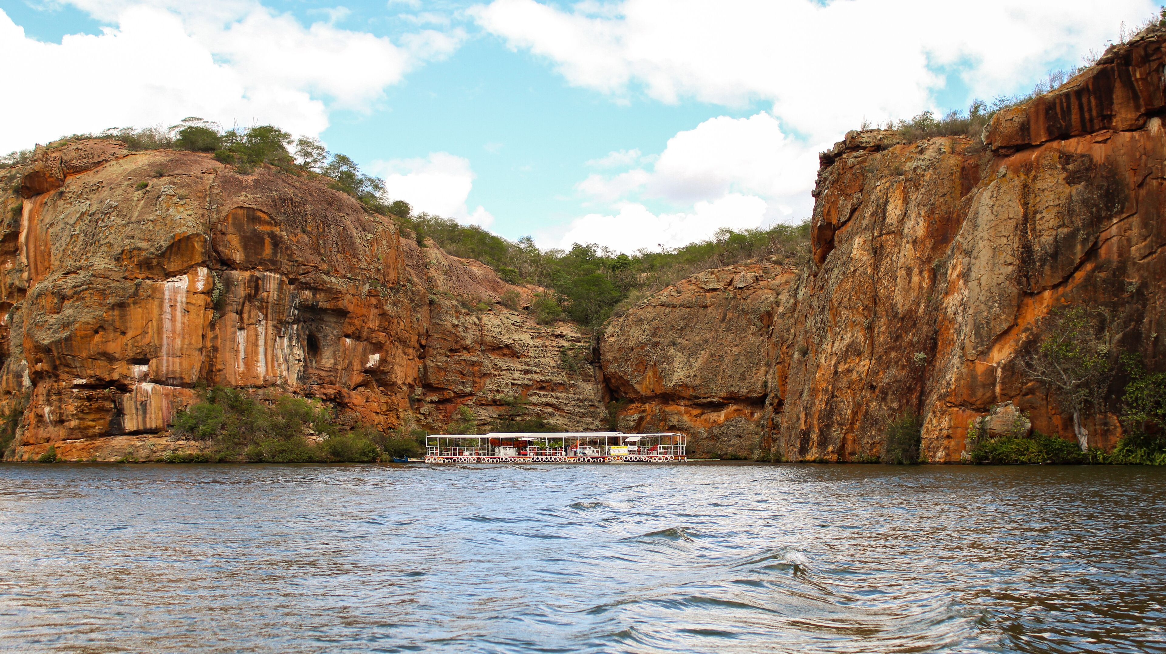 A river with a boat in the middle, surrounded by rocky cliffs and greenery.