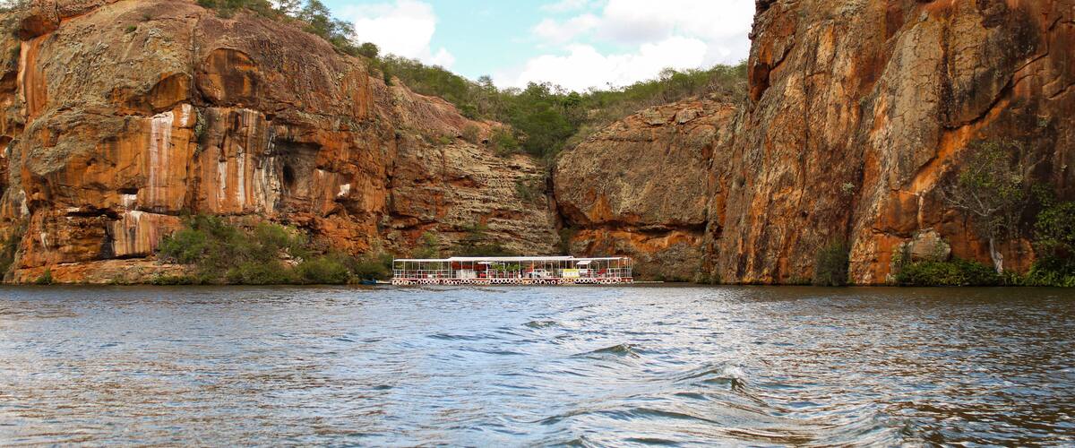 A river with a boat in the middle, surrounded by rocky cliffs and greenery.