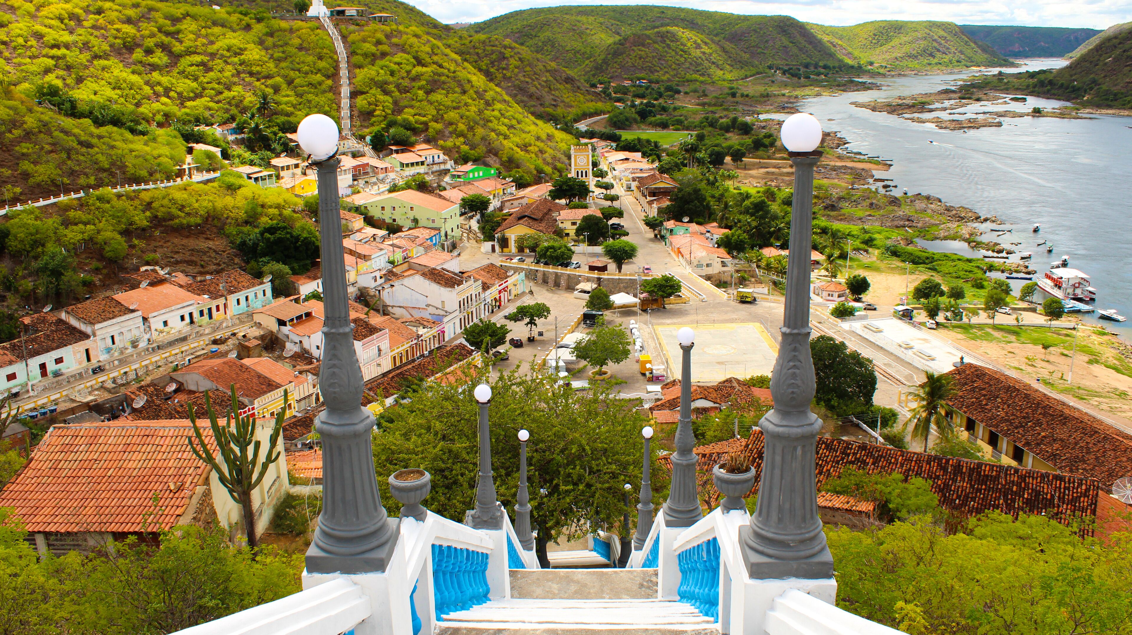 A town with colorful buildings, a river, and a staircase with street lamps.