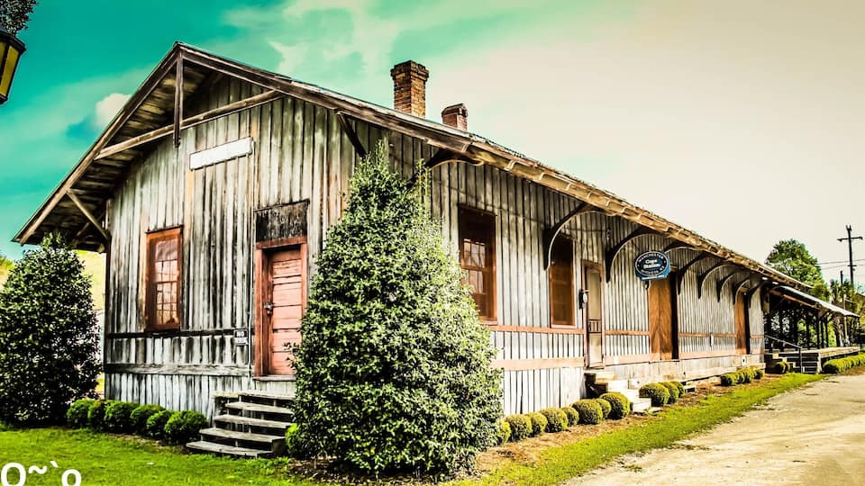 A rustic wooden building with a porch, a sign reading "Matchless Station," and a small tree in front.