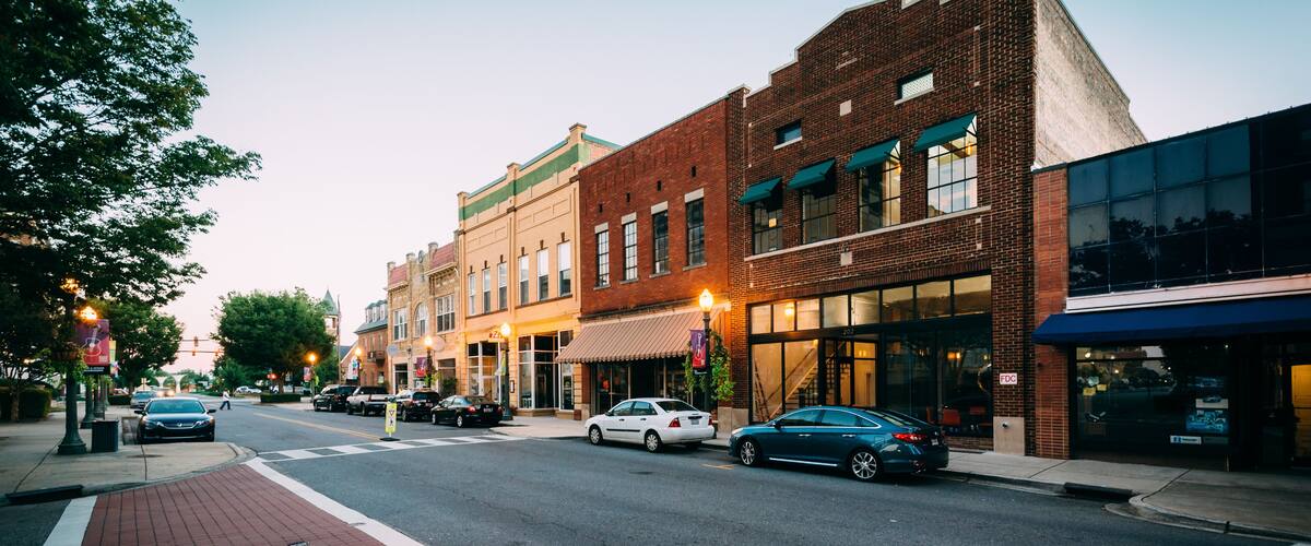 A street lined with historic buildings, a crosswalk, and cars parked along the road.