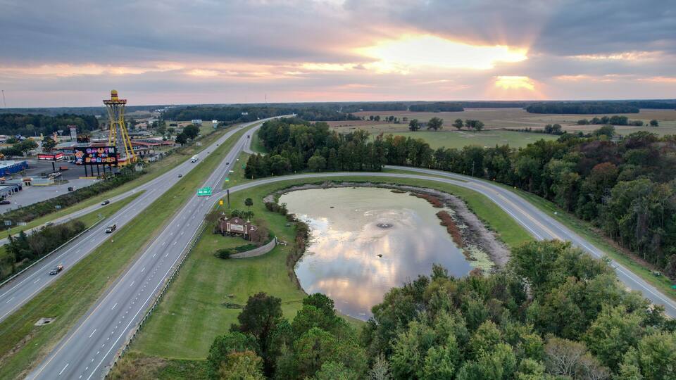A highway curving around a pond with a ferris wheel in the background.