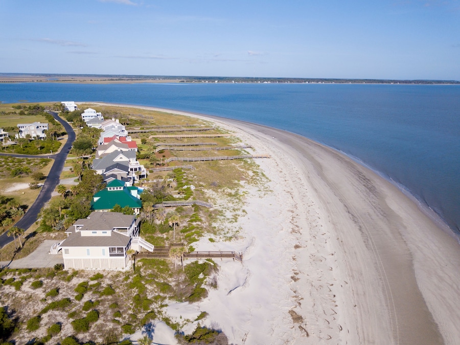 A coastal residential area with houses along a sandy beach and a clear blue ocean.