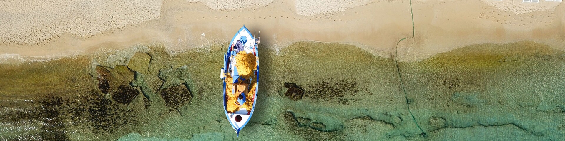Vista aérea de una playa con tumbonas y sombrillas, un barco en el agua y aguas claras y poco profundas.