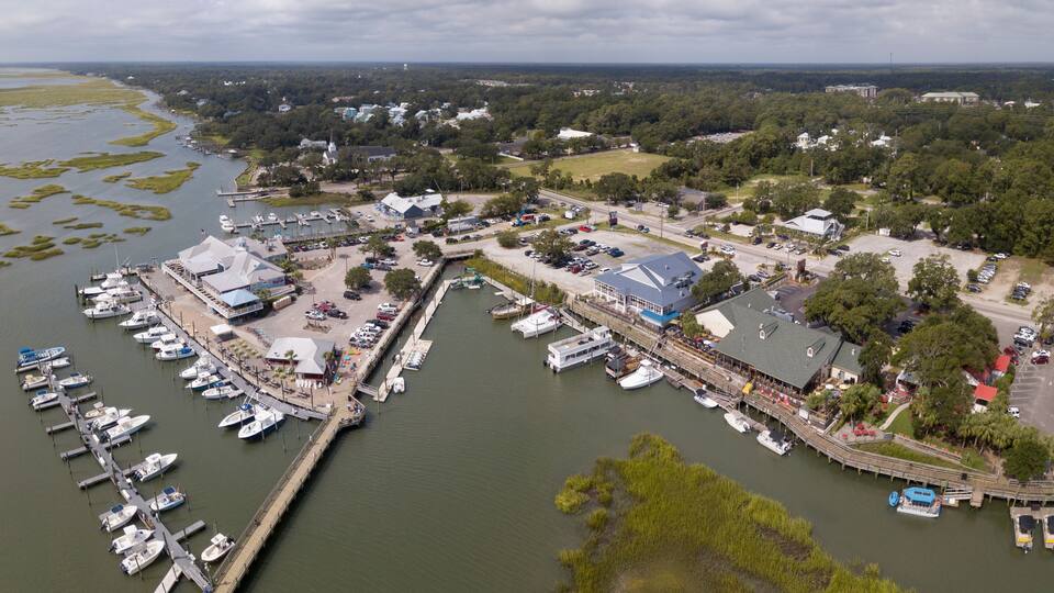 An aerial view of a marina with boats docked, surrounded by greenery and buildings.