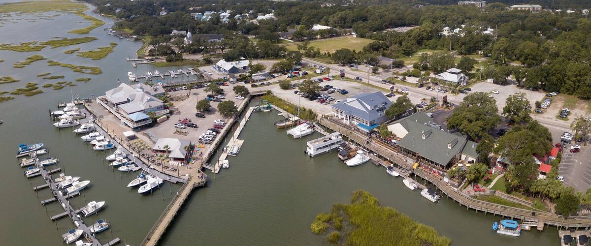 An aerial view of a marina with boats docked, surrounded by greenery and buildings.