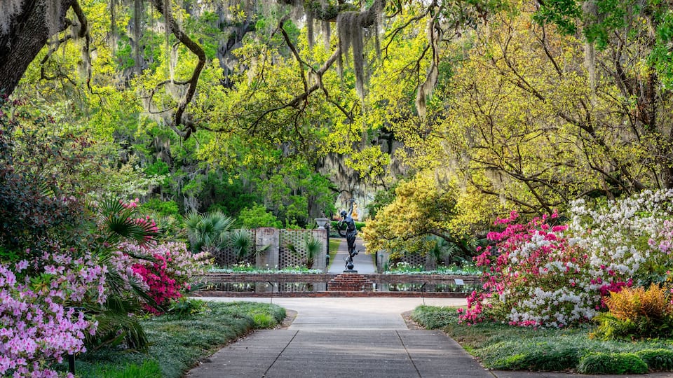 A garden with a statue, lush greenery, and flowering plants.