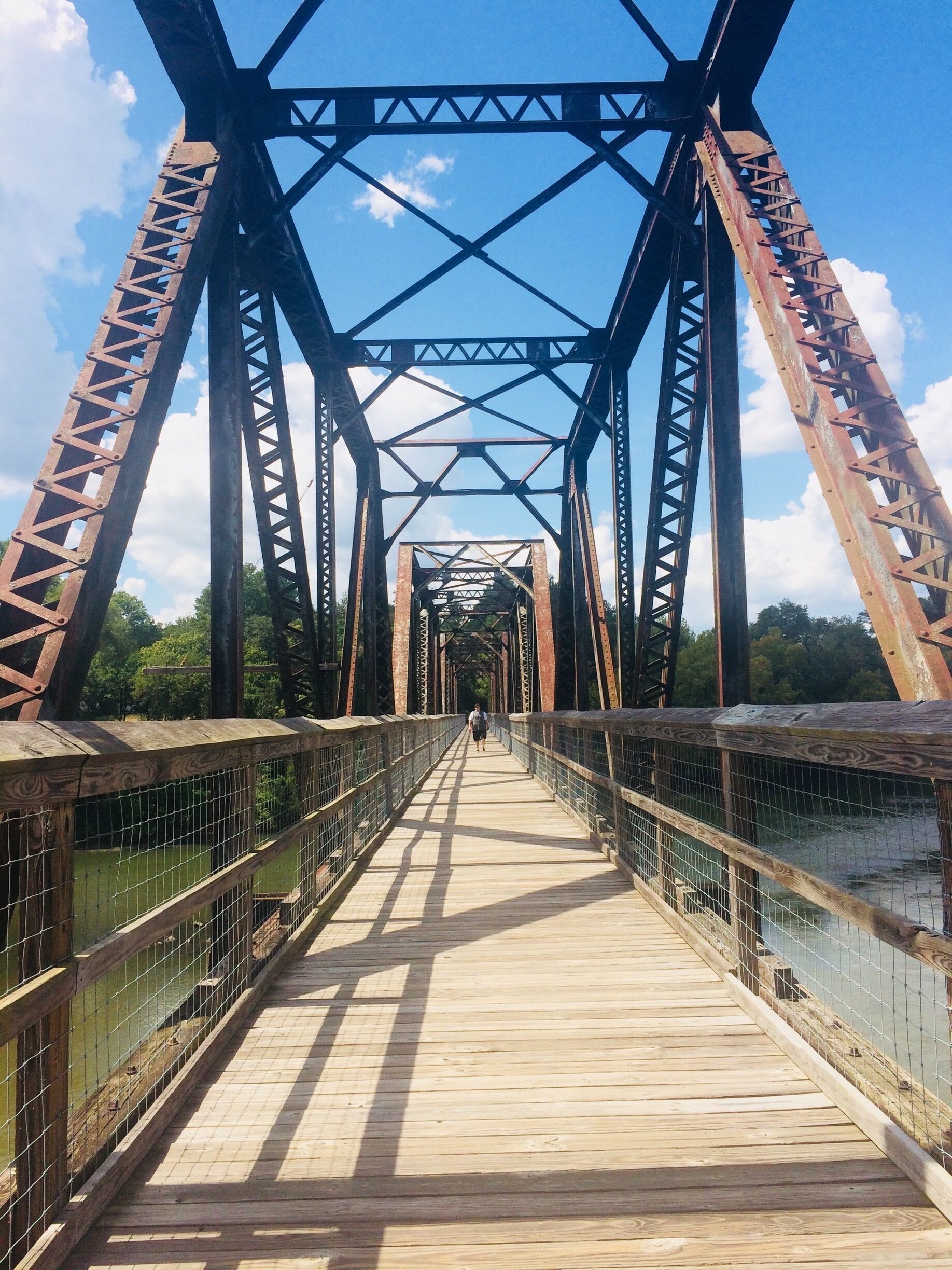 A wooden pedestrian bridge with metal trusses spanning a body of water.