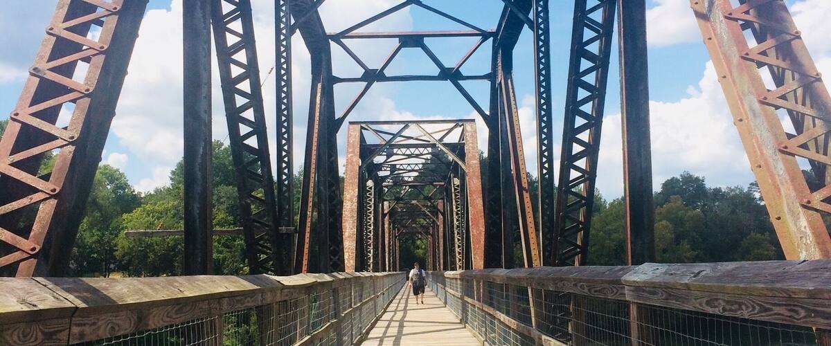 A wooden pedestrian bridge with metal trusses spanning a body of water.