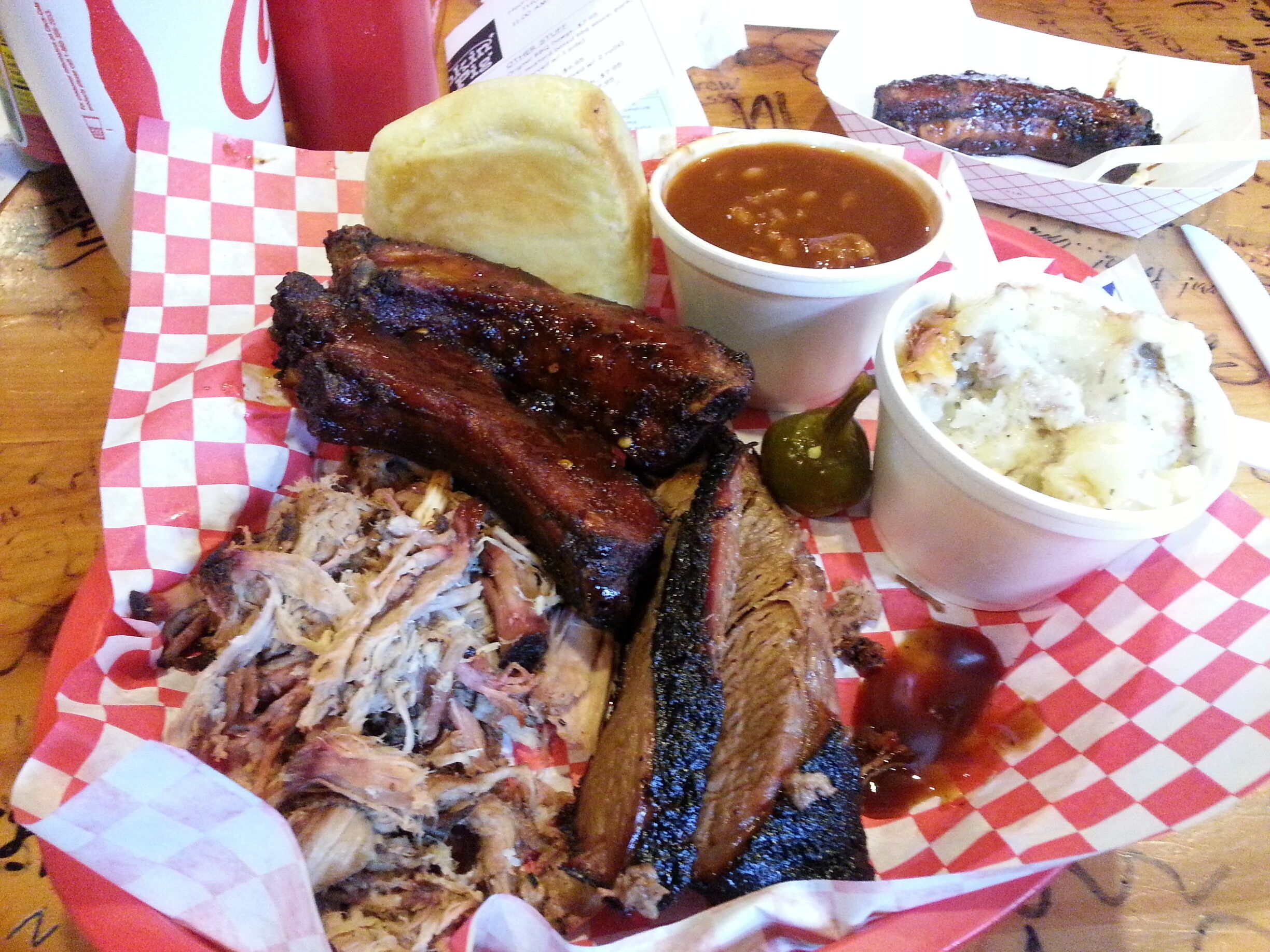 A plate of barbecued ribs, beans, coleslaw, and a biscuit.