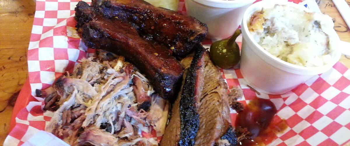 A plate of barbecued ribs, beans, coleslaw, and a biscuit.