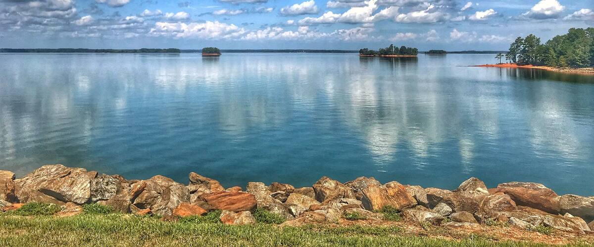 A calm lake with clear blue water, surrounded by rocky shores and small islands with trees.