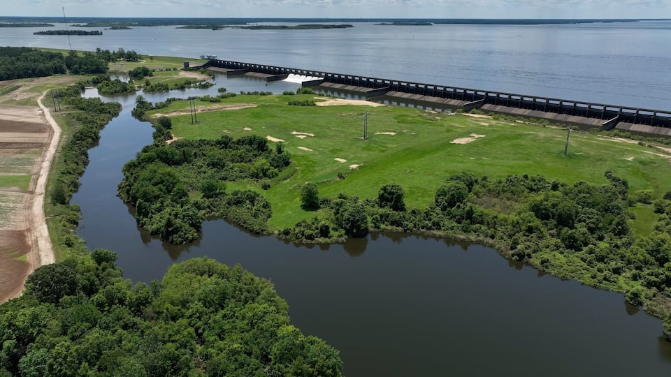 A river with a dam and a bridge, surrounded by greenery and fields.