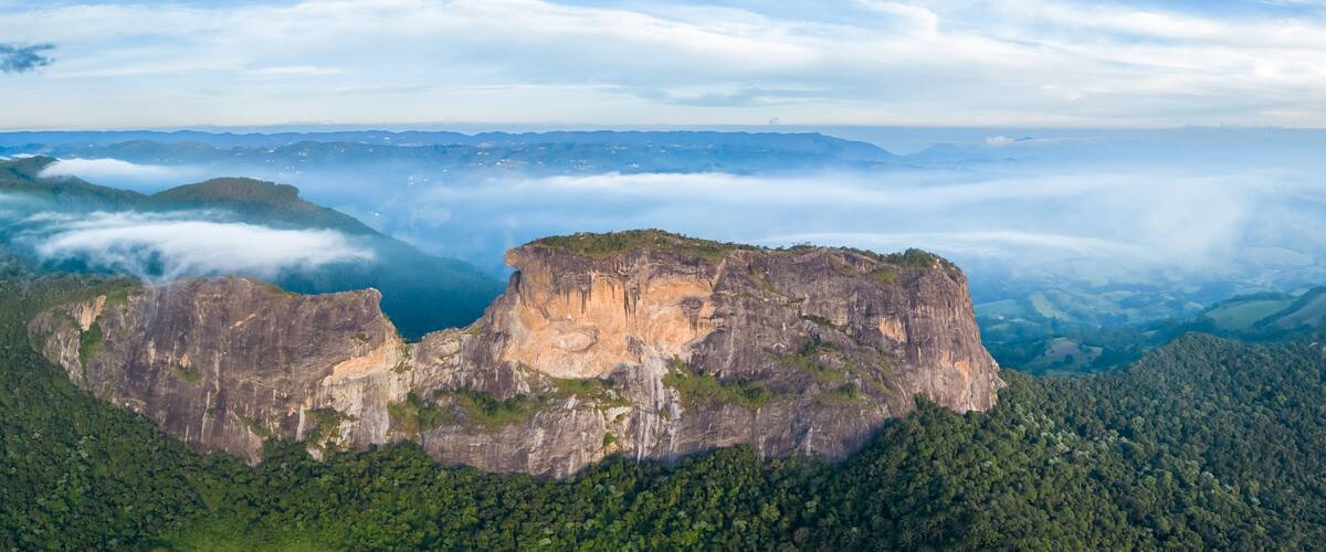 A rugged cliff formation surrounded by dense forest and mist-covered valleys.