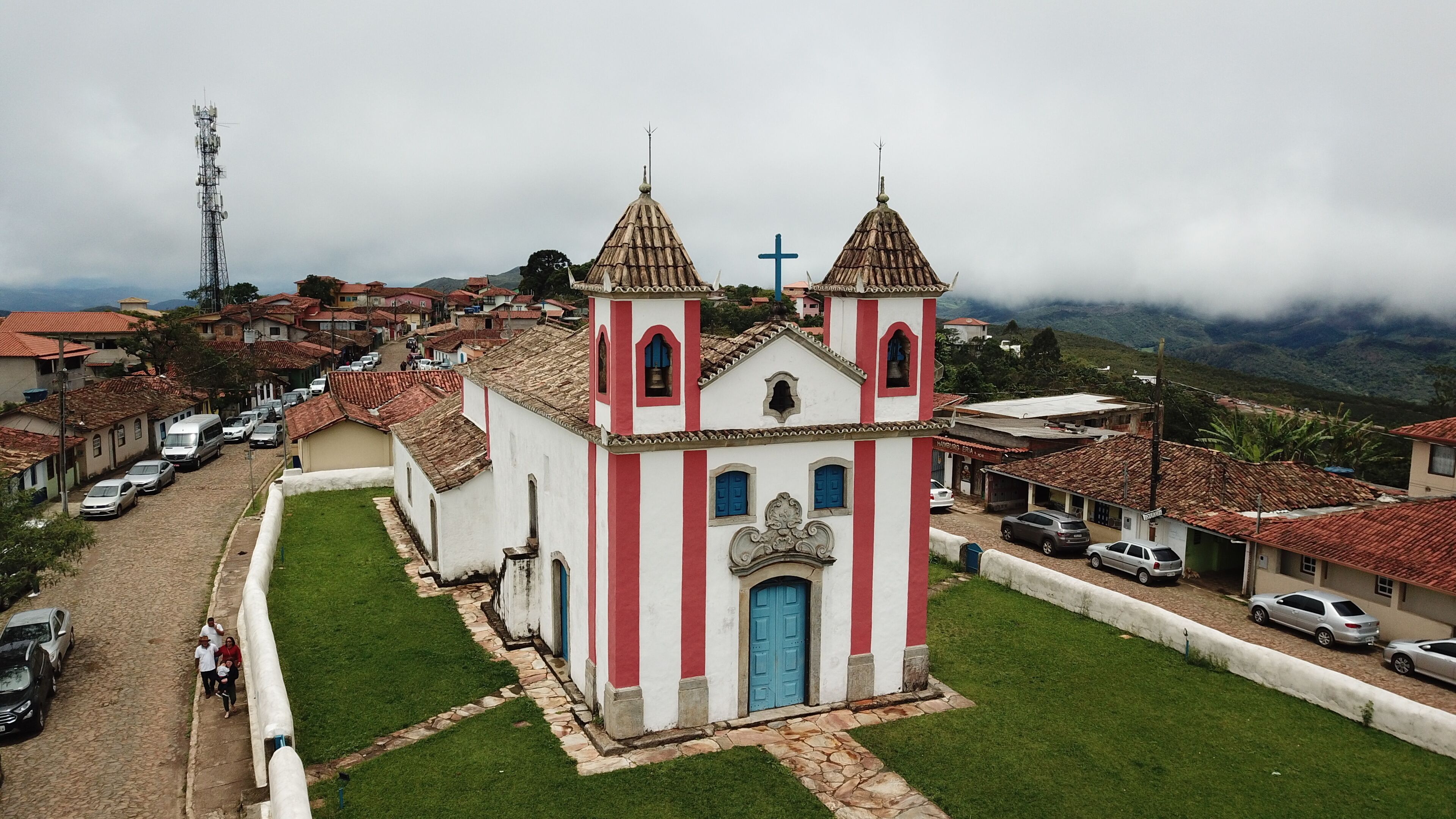 A church with a cross on top, surrounded by a cobblestone street and parked cars.
