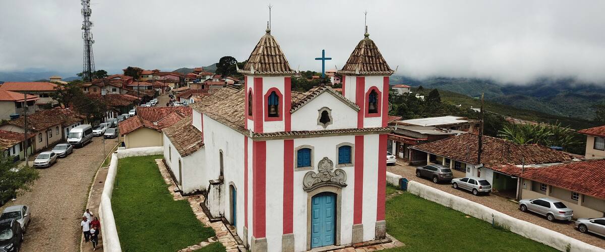 A church with a cross on top, surrounded by a cobblestone street and parked cars.