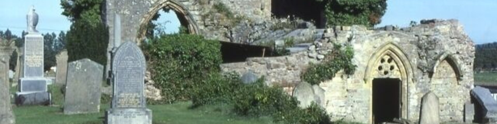 Una estructura de piedra histórica con un arco de entrada y lápidas alrededor.