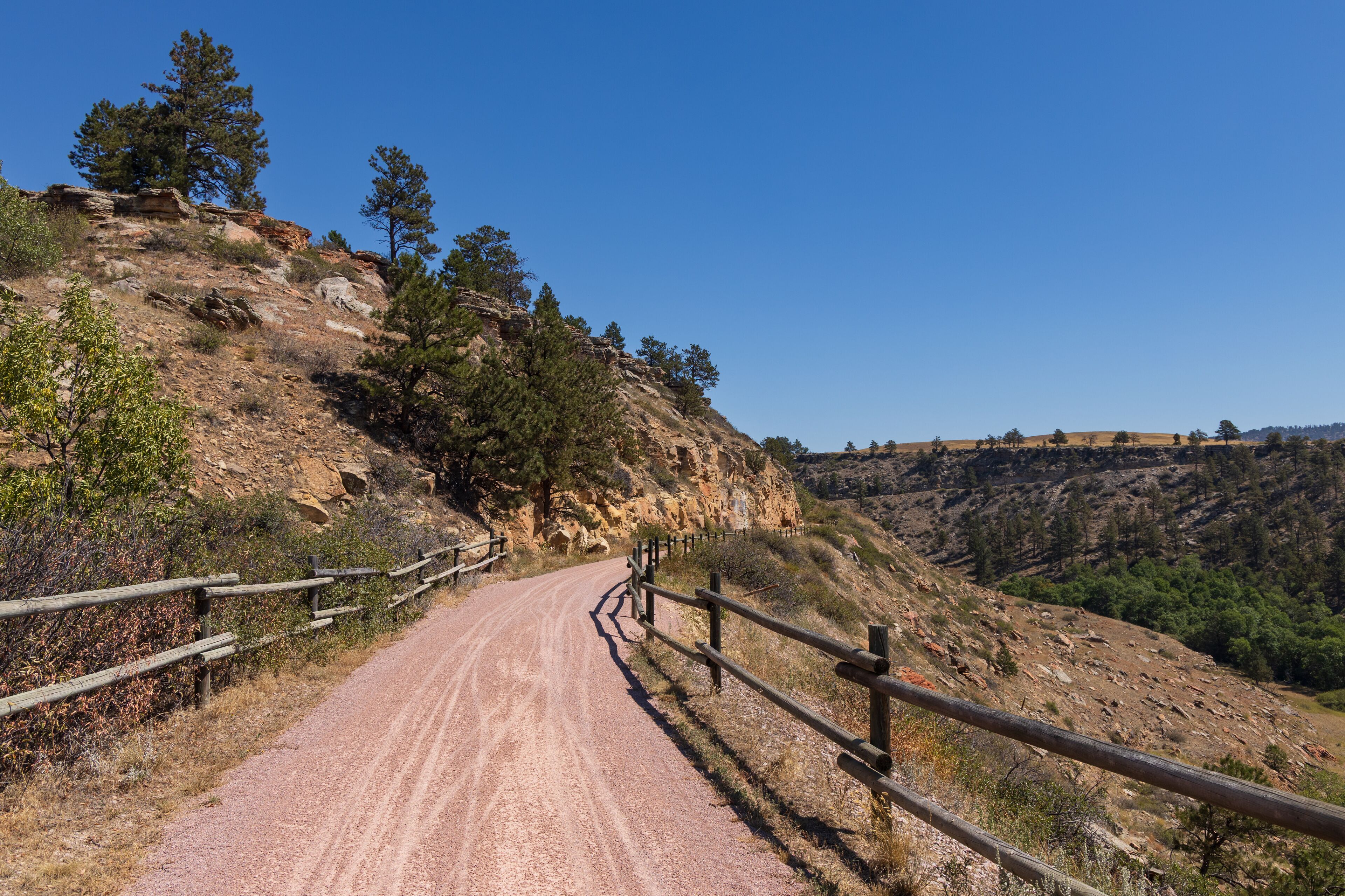A dirt road winding through a rocky hillside with sparse vegetation and wooden guardrails.