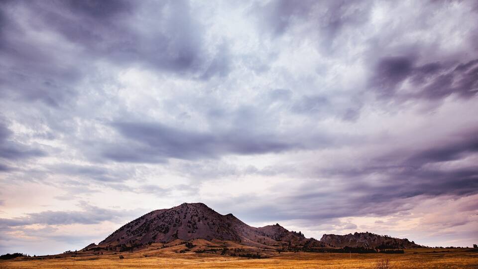 A mountainous landscape with a field in the foreground and a cloudy sky.