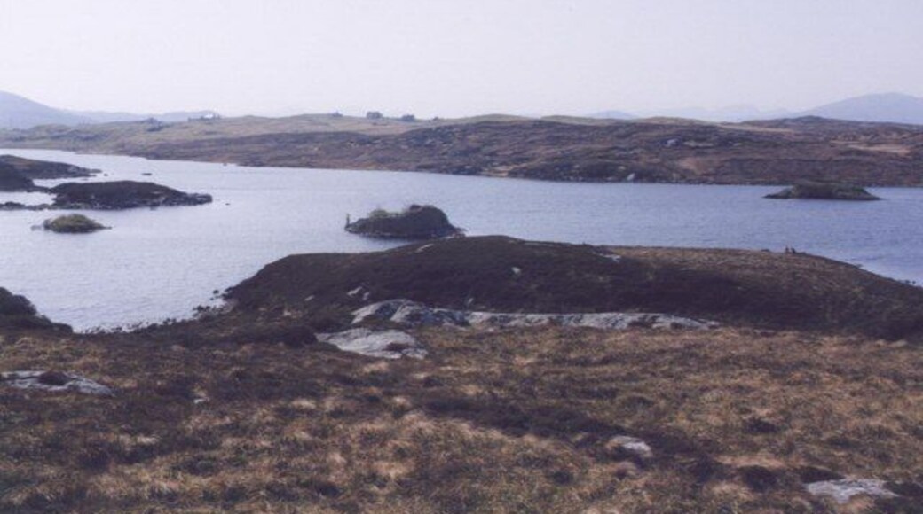 Loch Barabhat and Dun. The dun in loch Barabhat with the crofts of Tacleit beyond. Featuring a fisherman and some rough moorland.