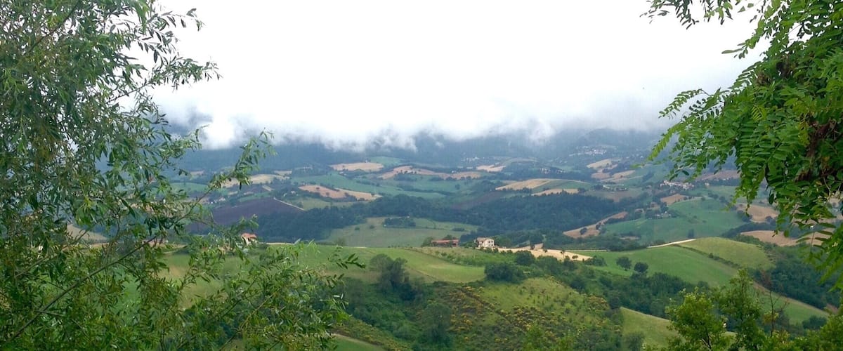 A lush valley with rolling hills, scattered houses, and dense greenery.
