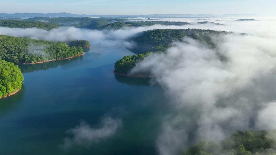 A lake surrounded by forested hills and shrouded in morning mist.
