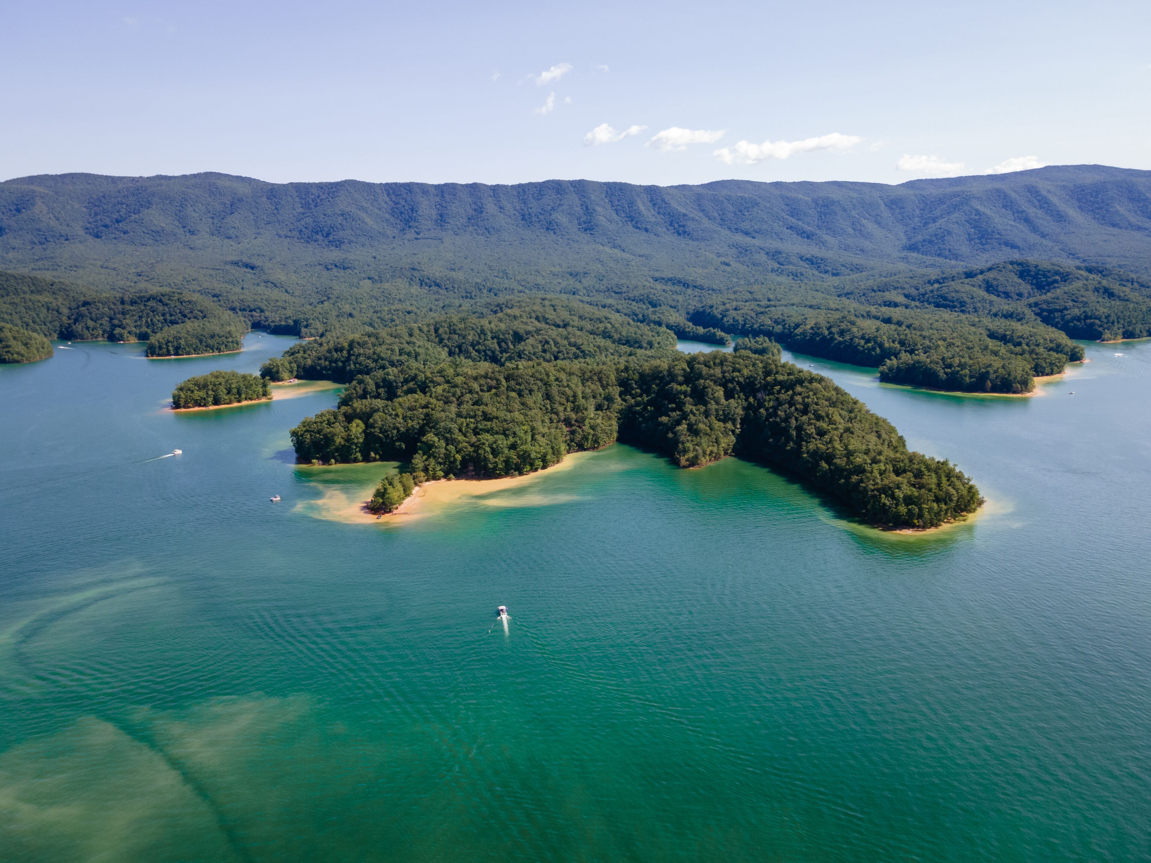 An aerial view of a series of forested islands surrounded by clear blue waters, with a hiker visible on one of the islands.