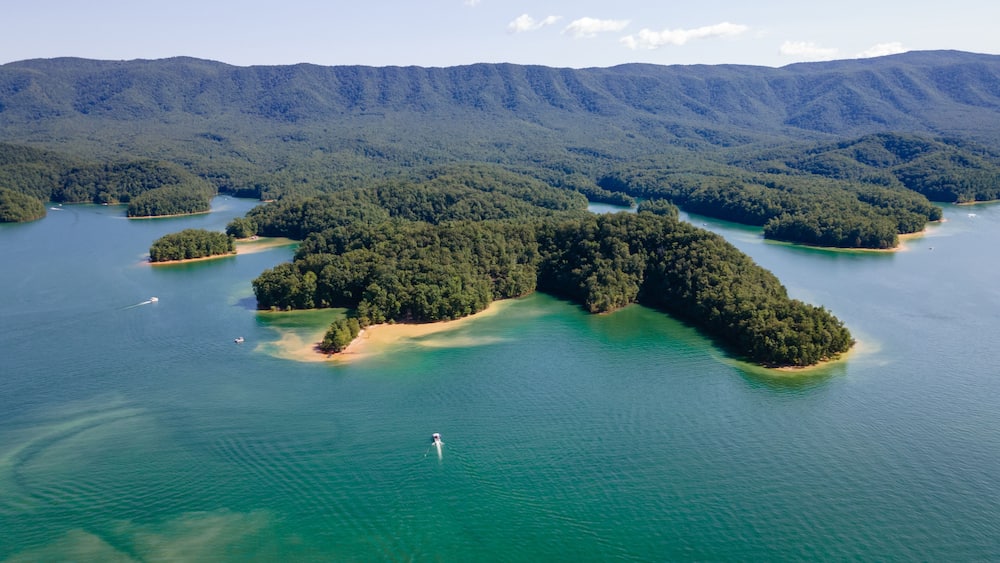 An aerial view of a series of forested islands surrounded by clear blue waters, with a hiker visible on one of the islands.