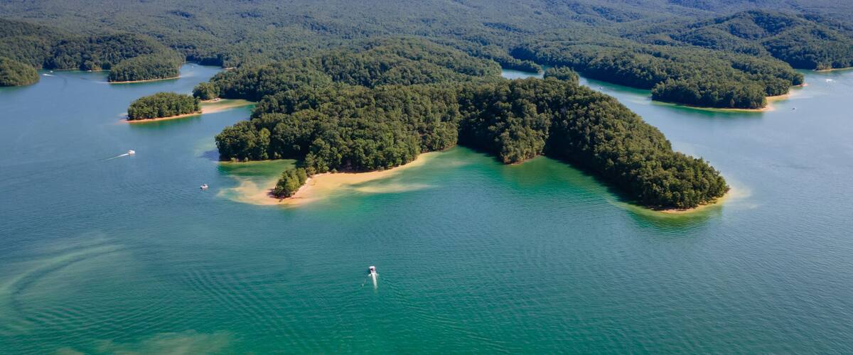 Vista aérea de una serie de islas boscosas rodeadas de aguas azul turquesa, con un excursionista visible en una de ellas.