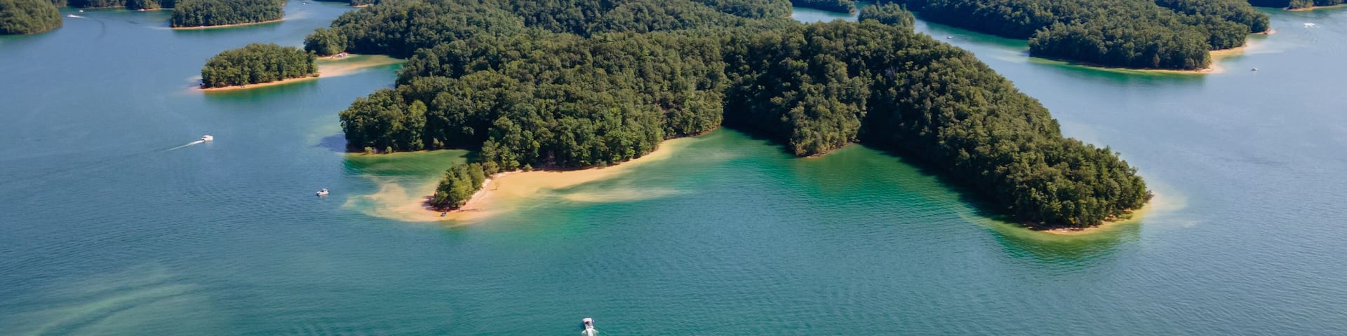 An aerial view of a series of forested islands surrounded by clear blue waters, with a hiker visible on one of the islands.