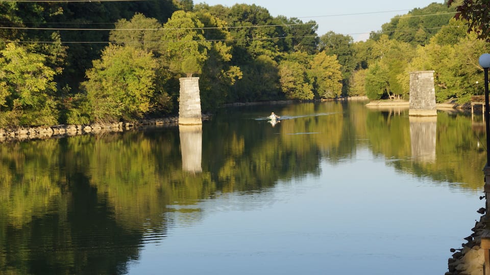 A calm river with a boat, surrounded by lush greenery and stone structures.