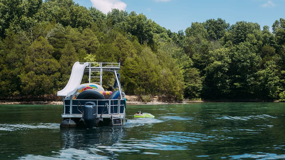 Woman floating next to pontoon boat in lake on summer day