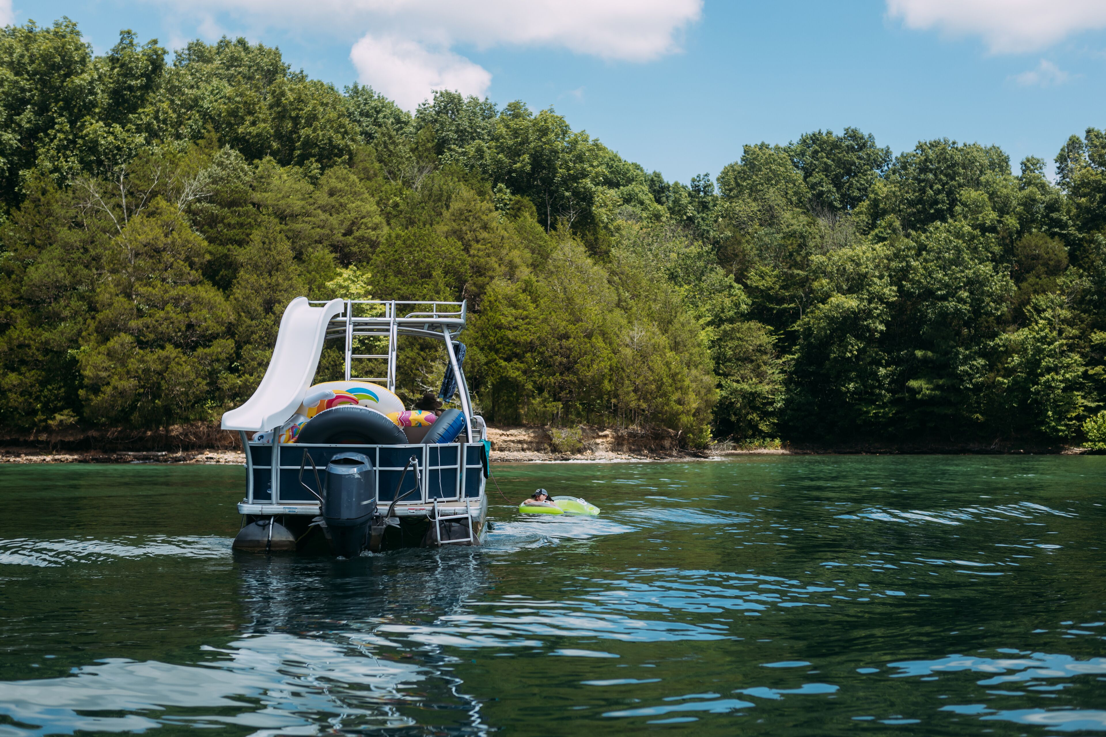 A watercraft with a slide and inflatable rings, floating on a calm river surrounded by dense forest.