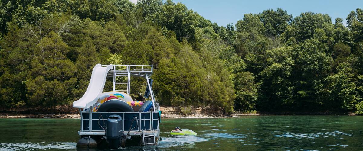 A watercraft with a slide and inflatable rings, floating on a calm river surrounded by dense forest.