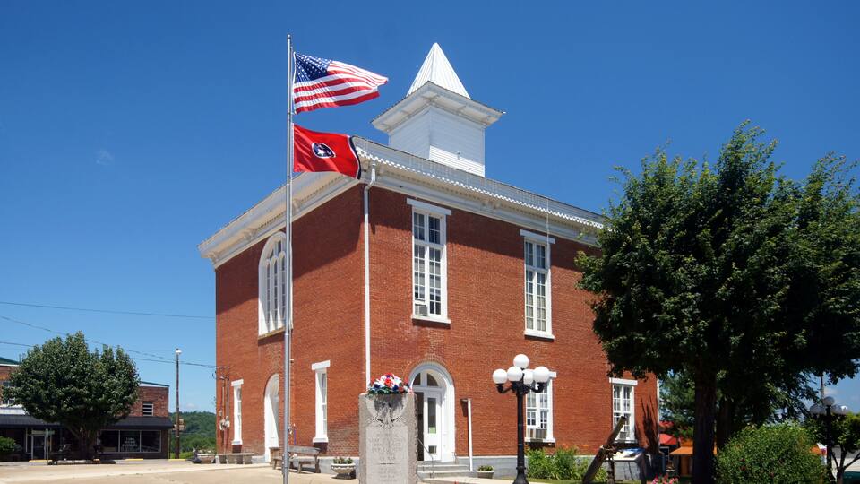 A red brick building with a white steeple, a flagpole with the American flag, and a Confederate soldier's headstone.