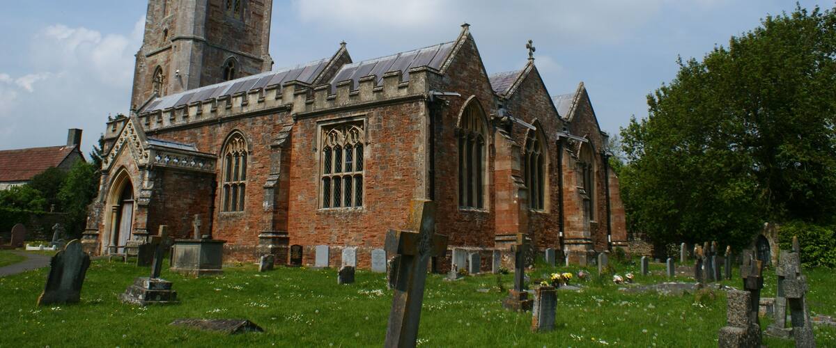 A historic church with a tall spire and a cemetery in front.