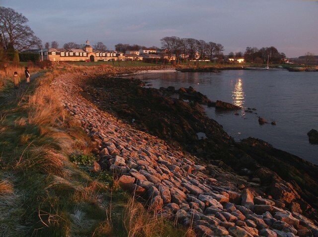 A riverside path with a stone wall, a body of water, and a building in the background.