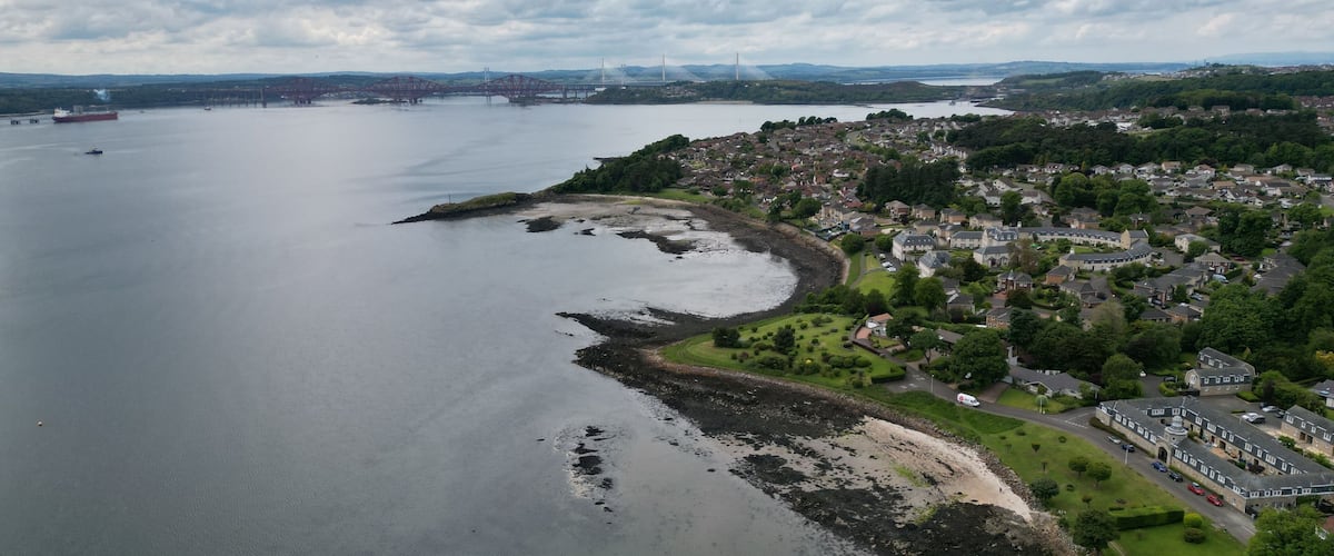 A coastal town with a harbor, a bridge, and a distant wind turbine.
