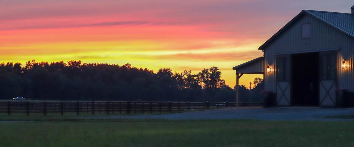 A barn at sunset with a colorful sky.