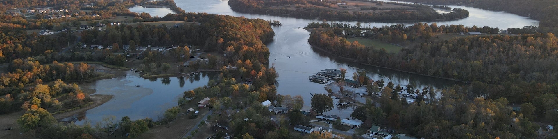 An aerial view of a river winding through a forested area with several buildings and a small lake.