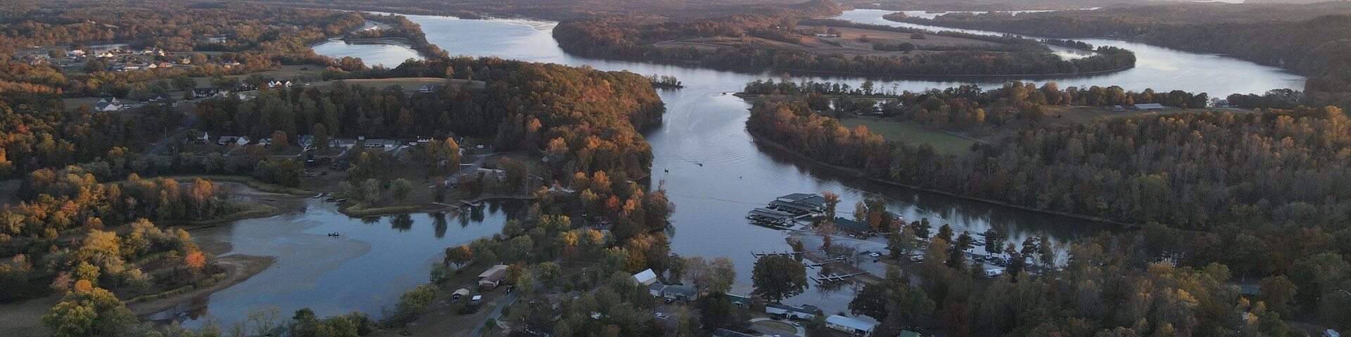 Vista aérea de un río serpenteando a través de una zona boscosa con varios edificios y un pequeño lago.