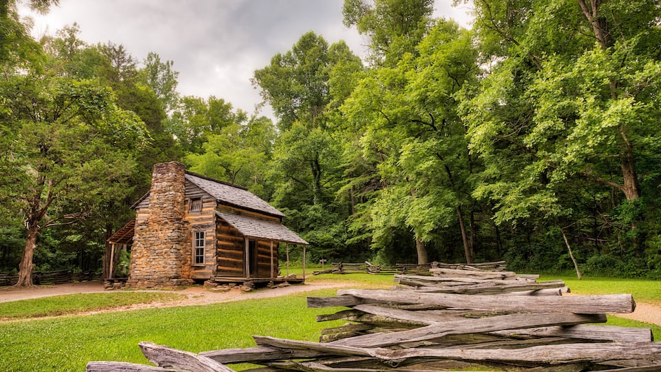 A rustic stone cabin surrounded by lush green trees and a wooden fence.